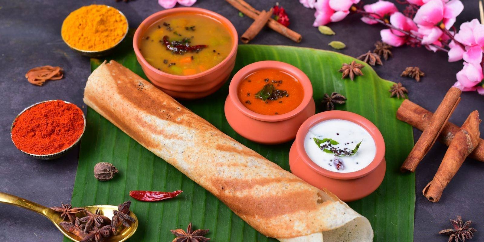 Crisp golden dosa rolled on a banana leaf with sambar and chutneys